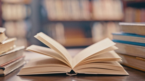 Several books on a table in the foreground with shelves full of books in the background.